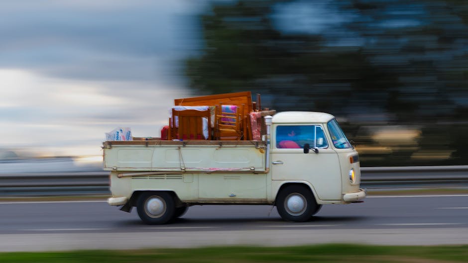 A yellow van with severe front-end damage, including a crumpled hood and shattered windshield, is positioned amidst debris in a site of destruction. The vehicle's paint appears scratched and dented, w